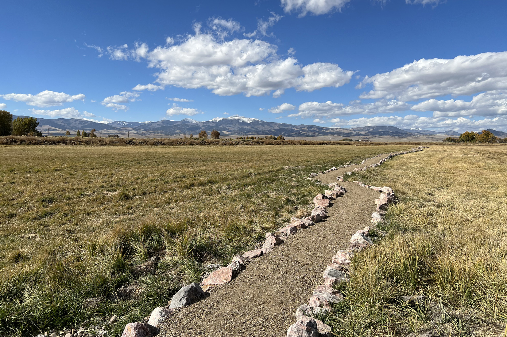 well-maintained trail, lined with sines, leads across flat land toward mountains